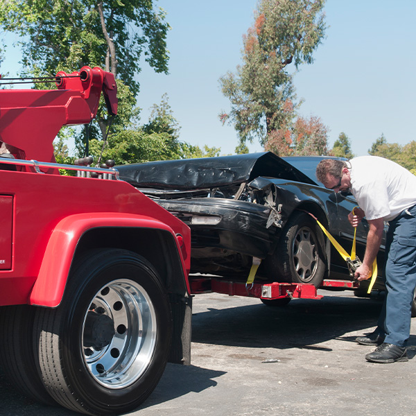 Tow truck driver securely strapping a wrecked car in preparation for towing it