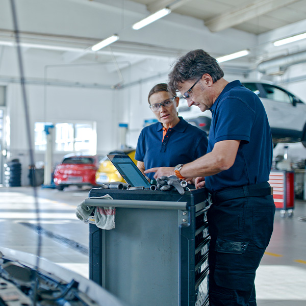 Manager and mechanic conducting a thorough inspection of a car engine using laptop